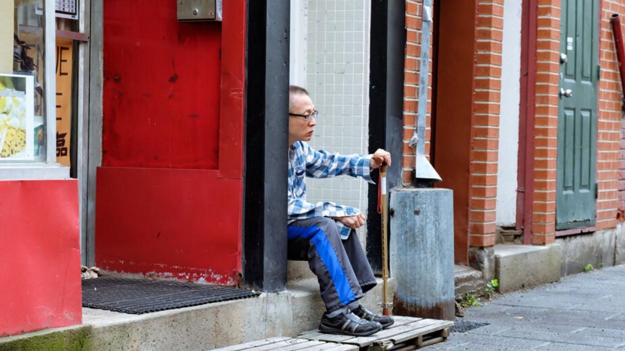 A person sits on a step holding a walking stick in Montreal's Chinatown.