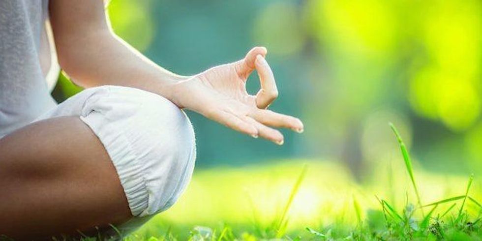A person sitting on grass with their legs crossed in a yoga pose. \u200b