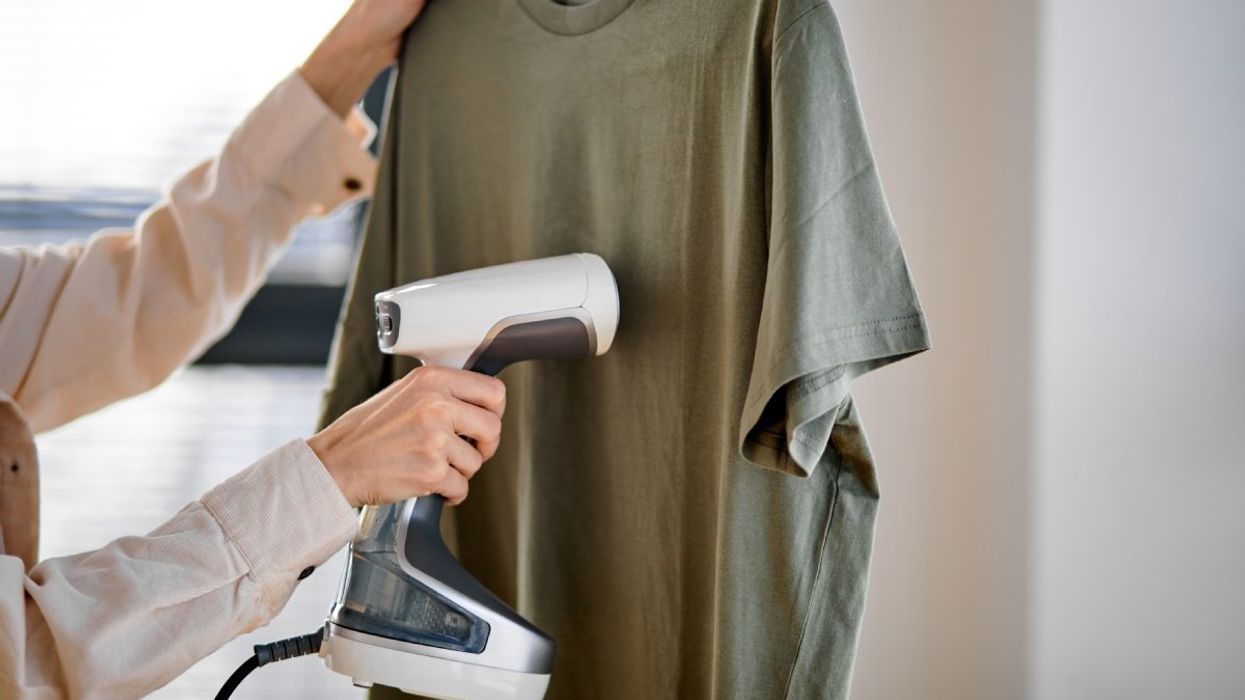 A person using a handheld steamers to remove wrinkles from a green t-shirt.