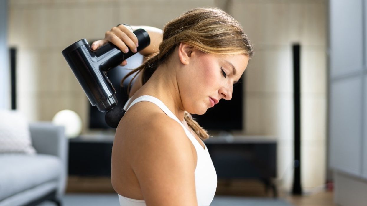 A person using a personal handheld massage gun on their back.