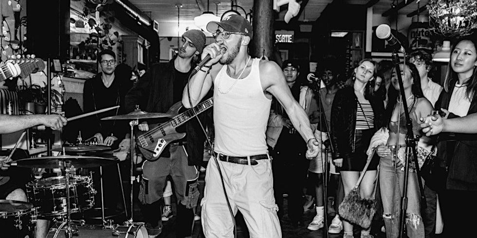 A person wearing a white tank top performing on stage in a Montreal bar as others look and watch.