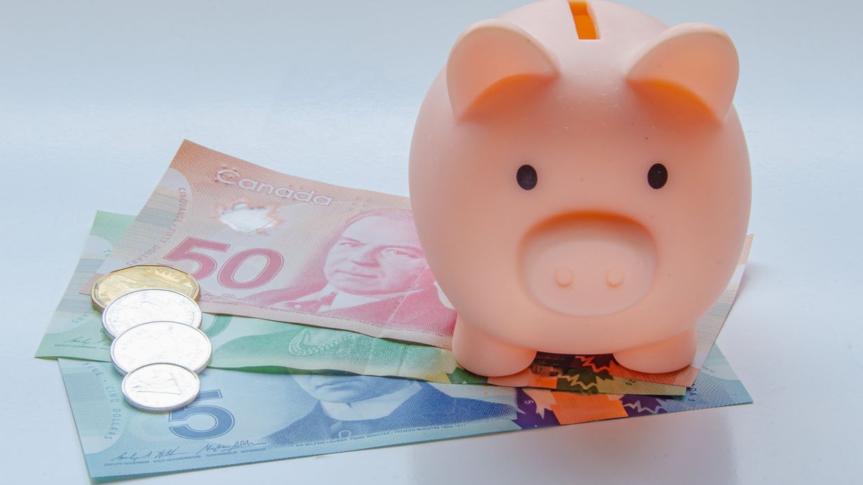 A piggy bank on top of various Canadian bills and coins.