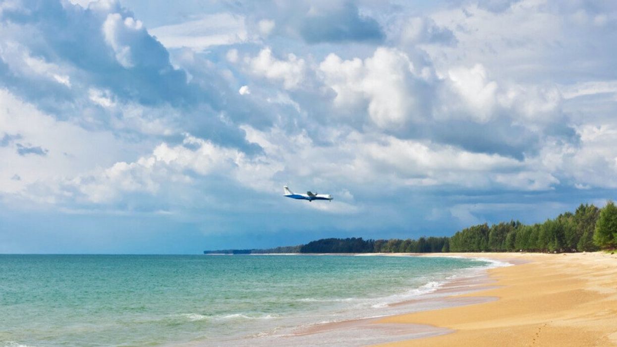 A plane flies over a beach.