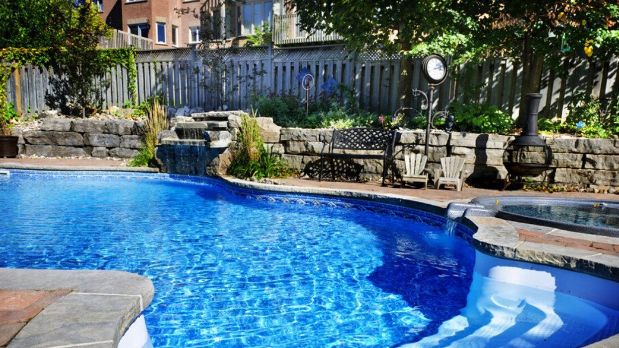 A residential inground swimming pool in backyard with waterfall and hot tub.