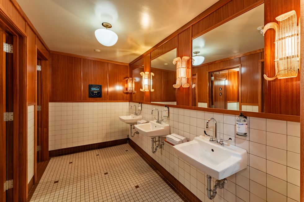 A restaurant bathroom with while tiles, wood walls and white basins.