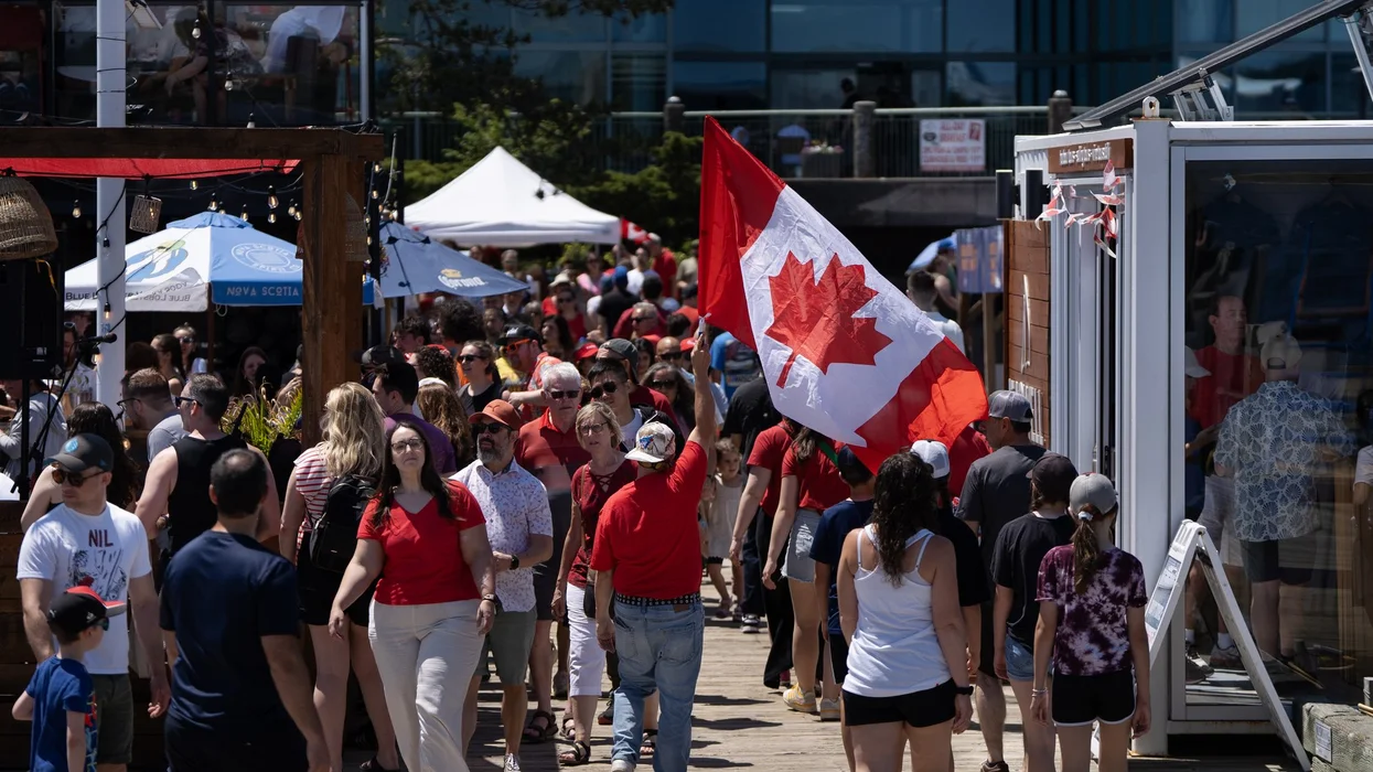 A reveller carries a Canada flag through a crowd on the Halifax Waterfront during Canada Day celebrations.