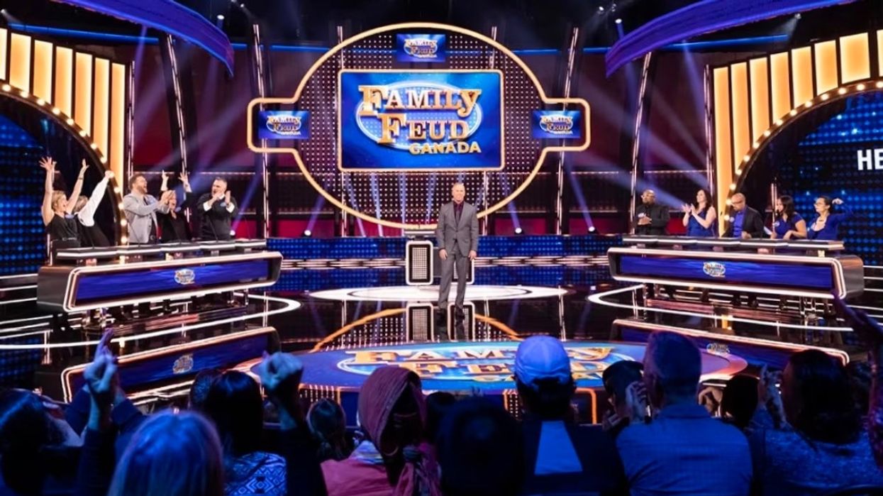 A screenshot from an episode of 'Family Feud Canada' with host Gerry Dee and two family's on the set/stage.