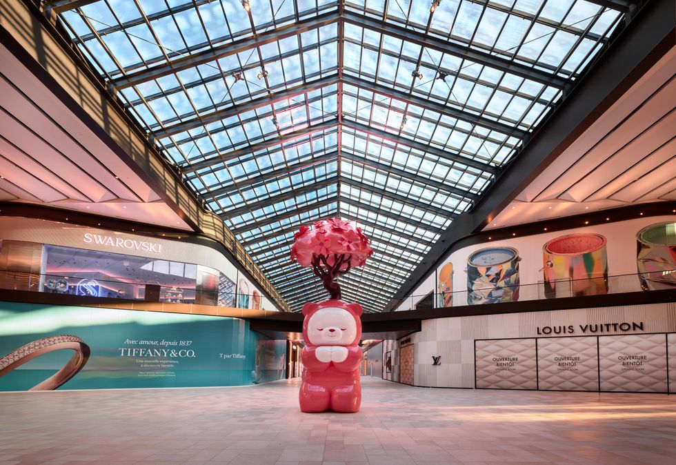 A sculpture of a red bear with a tree growing out of its head in the middle of a shopping centre atrium.