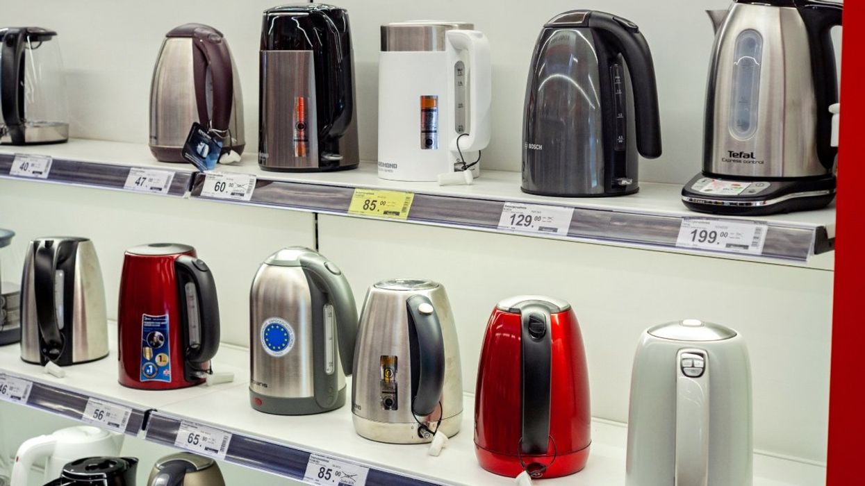 A series of electric kettles of various shapes and colours on multiple shelves in a department store. 