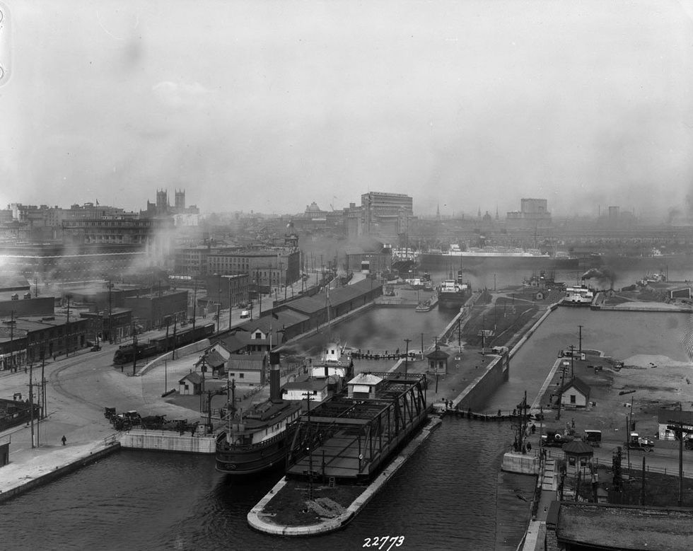 A ship enters the Lachine Canal from Montreal's Old Port. People waiting for the bridge to let them cross wait while a train can be seen moving along the railway.