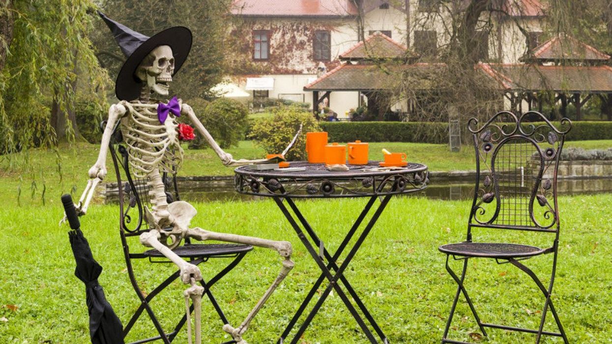 A skeleton wearing a witch hat and holding an umbrella in the rain.