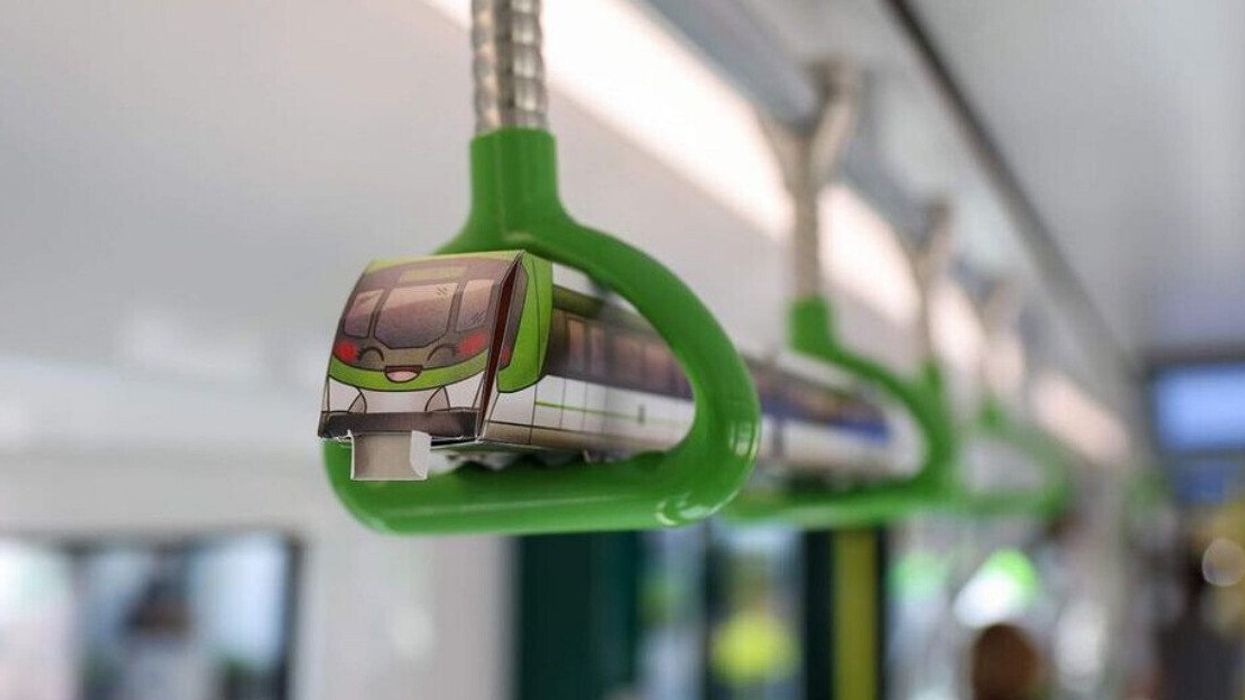 A smiling paper REM train hangs on hand holds in a car.