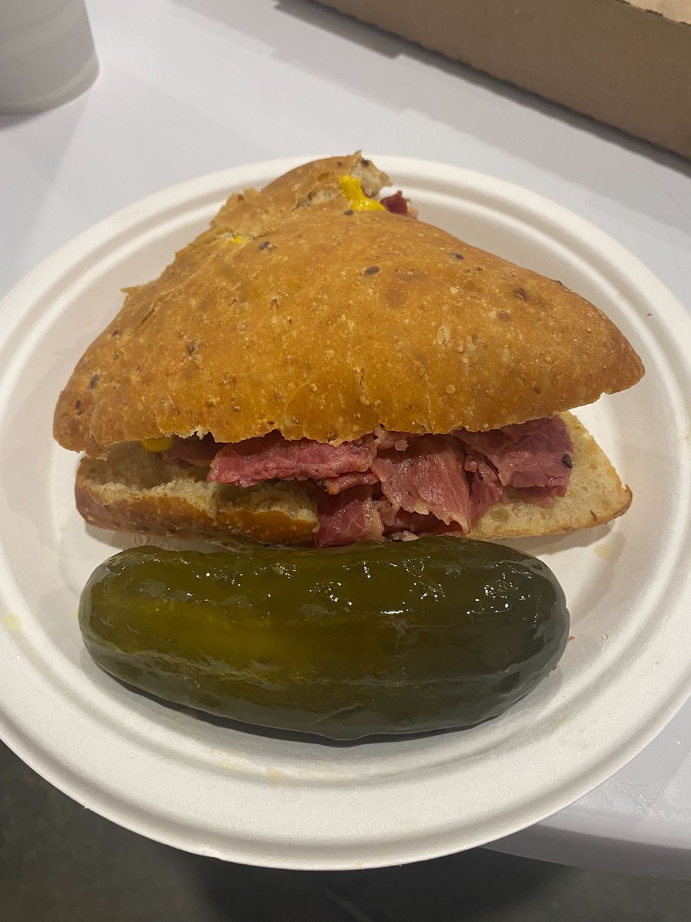 A smoked meat sandwich on a paper plate.