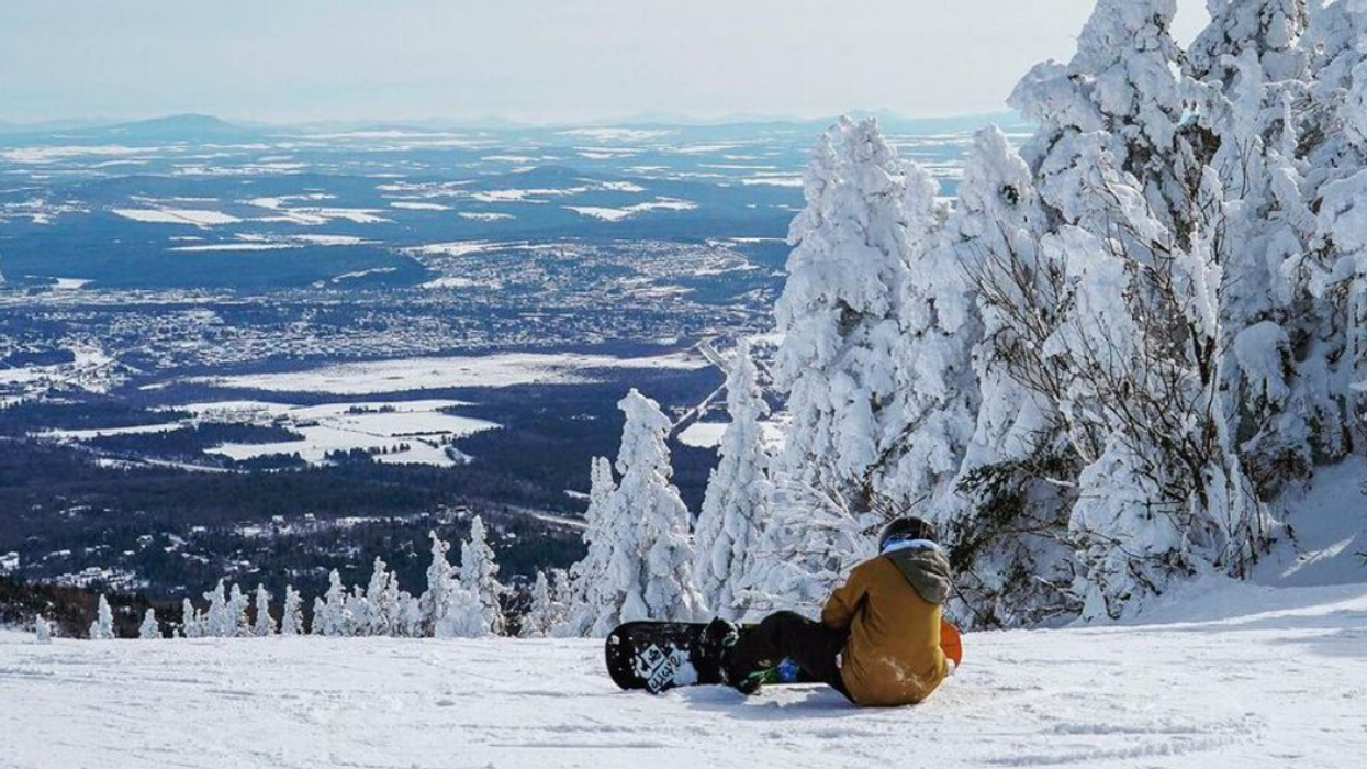 A snowboarder sits at the top of a mountain at Mont-Orford.