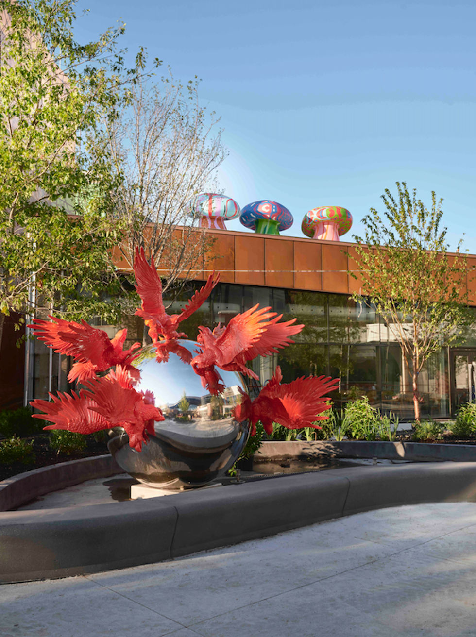 A steel ball with red bird sculptures on it, plus colourful mushroom sculptures atop a nearby bridge.