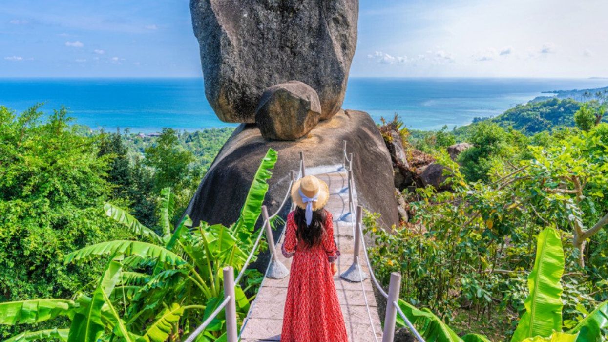 A tourist in a red dress and sunhat looks at the Overlap Stone in Koh Samui, Thailand.