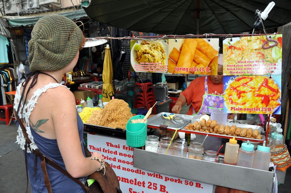 A tourist stops to buy Thai street food from a vendor on famed Khao San Road in Bangkok.