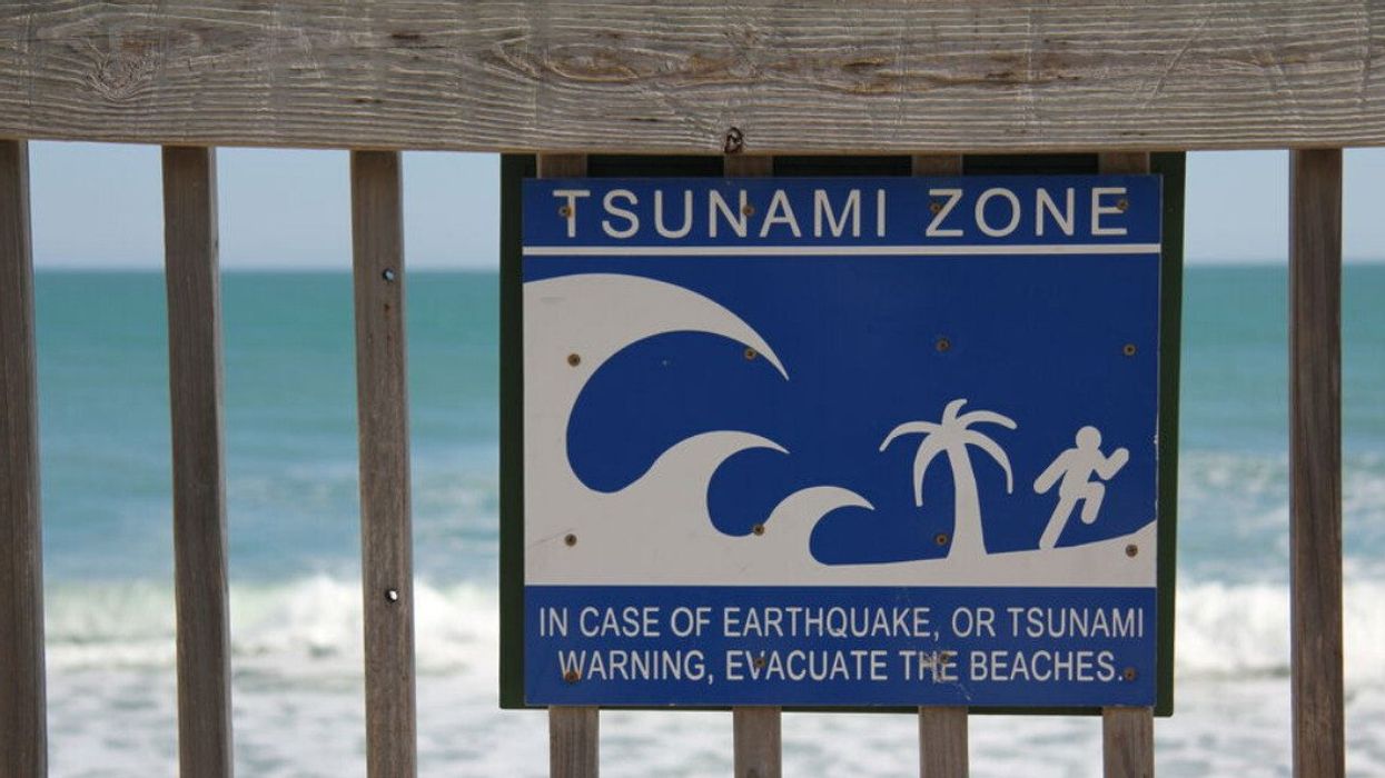 A tsunami zone sign that is attached to a wooden rail overlooking the Atlantic ocean in Florida.