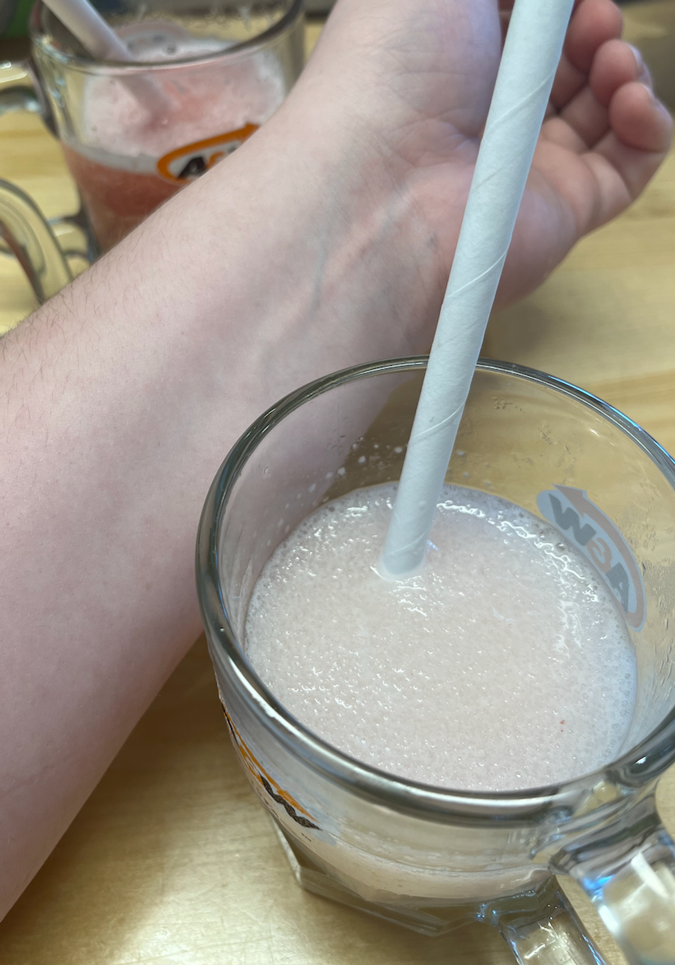 A very white arm next to a pinkish frozen lemonade concoction.