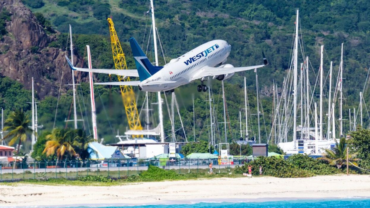 A Westjet plane flies over the beach toward the airport in Saint Maarten.