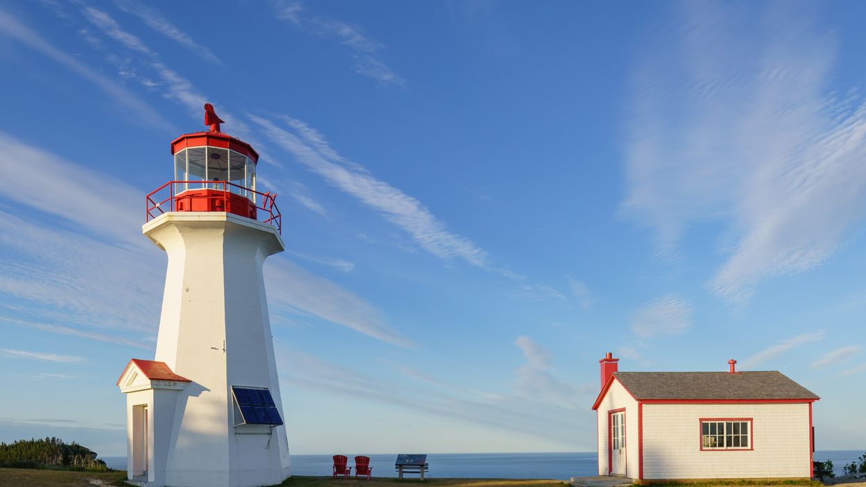 A white lighthouse and service house, both with red accents, on a peninsula overlooking the ocean.