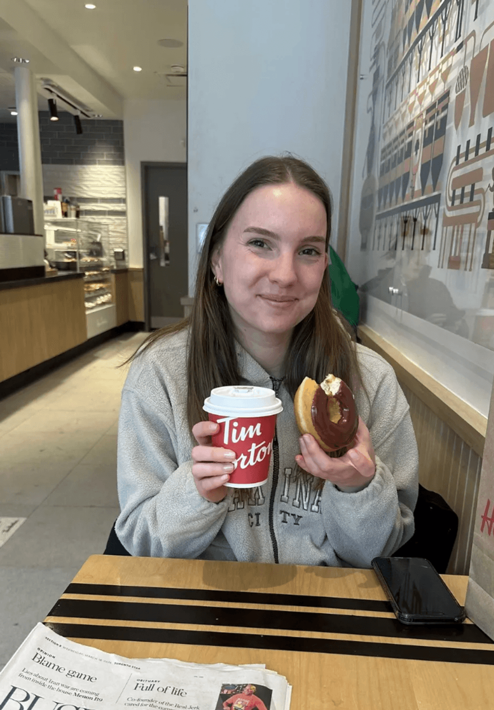A woman holdng a Tim Hortons coffee cup and a chocolate doughnut.