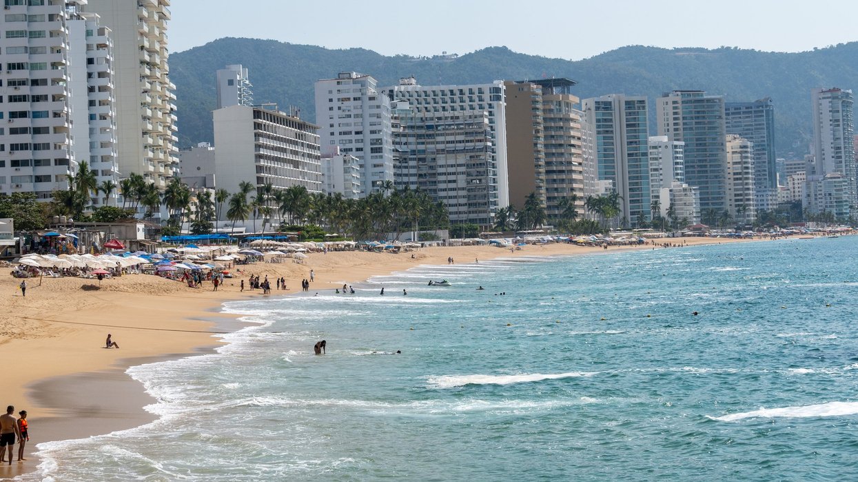 Acapulco, Mexico. Golden sand beach with people swimming and relaxing. Modern hotels line the vibrant oceanfront, backed by mountains.