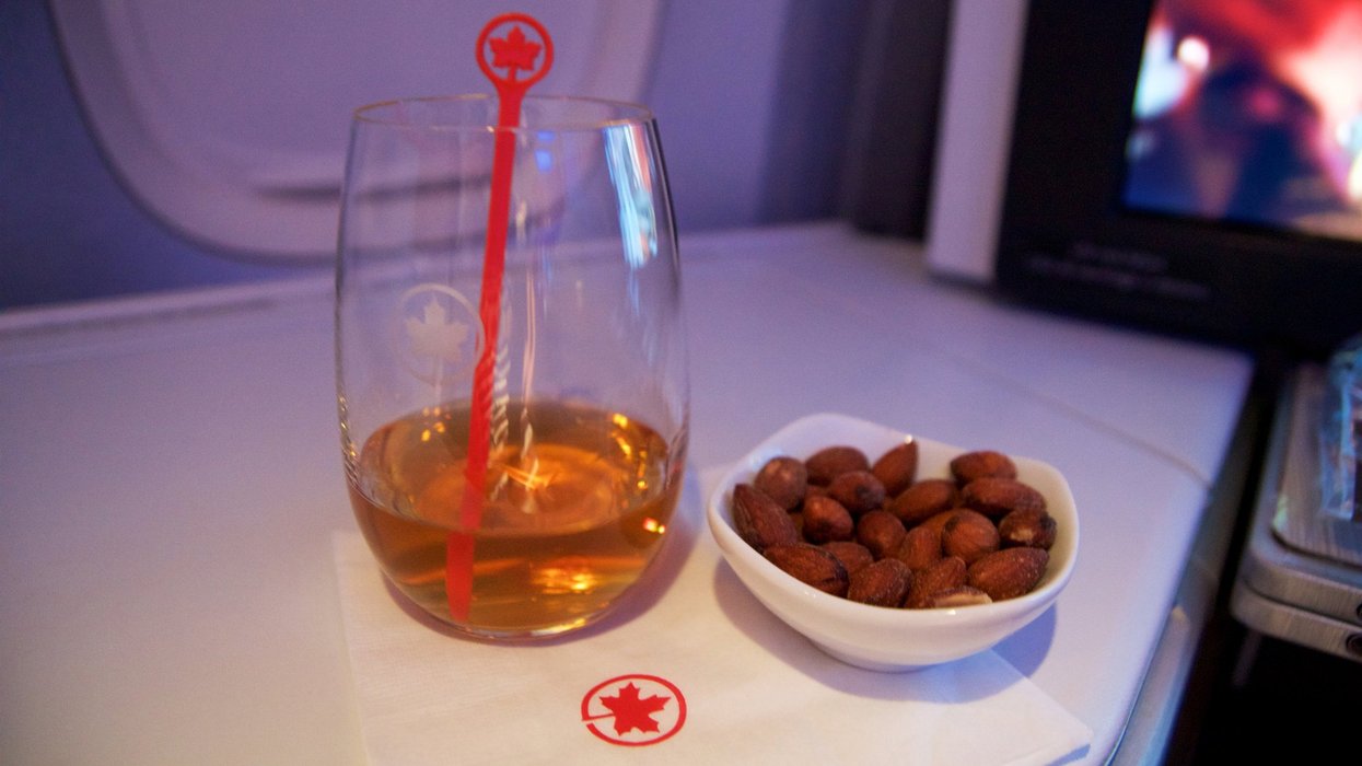 Air Canada Business class in a passenger plane. A glass of whisky and some warm nuts on a folding table inside a Boeing 777-300ER from AC.