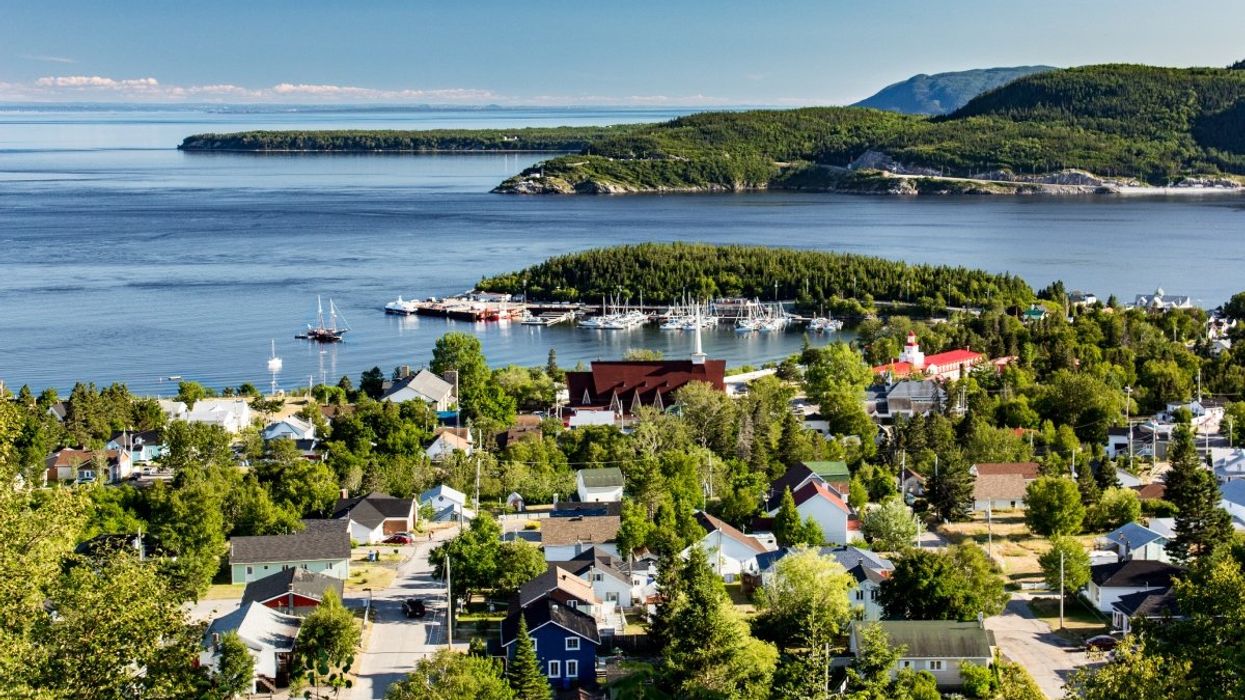 An aerial view of a village in Tadoussac with the St Lawrence River and mountains in the background.