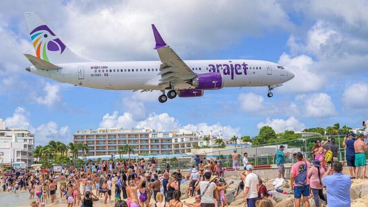 An Arajet plane in-flight over a beach, as onlookers snap photos.