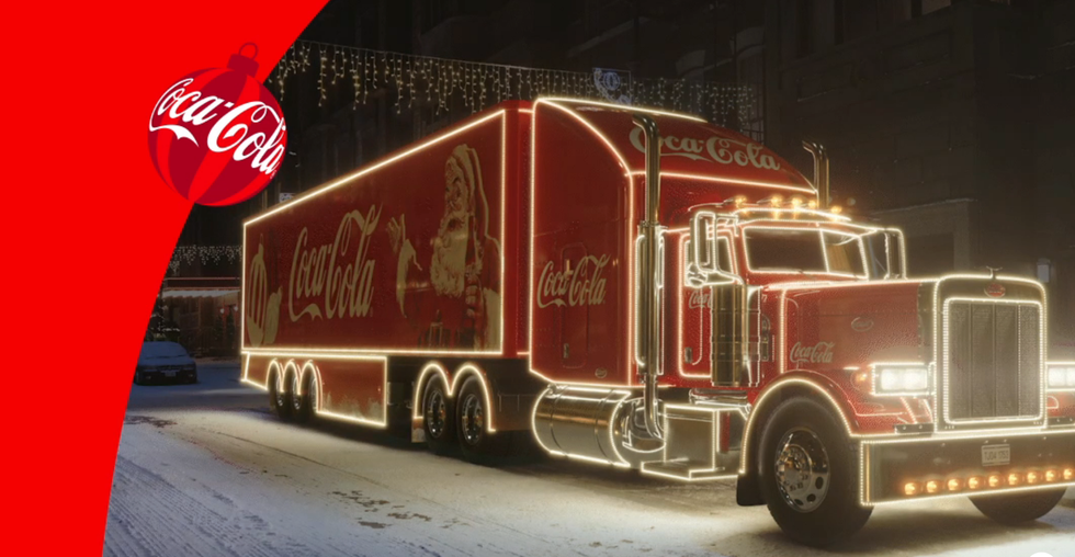 An illuminated Coca-Cola holiday truck decorated with lights on a snowy street.
