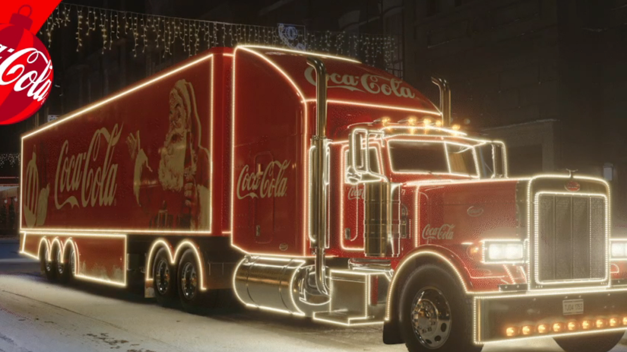 An illuminated Coca-Cola holiday truck decorated with lights on a snowy street.