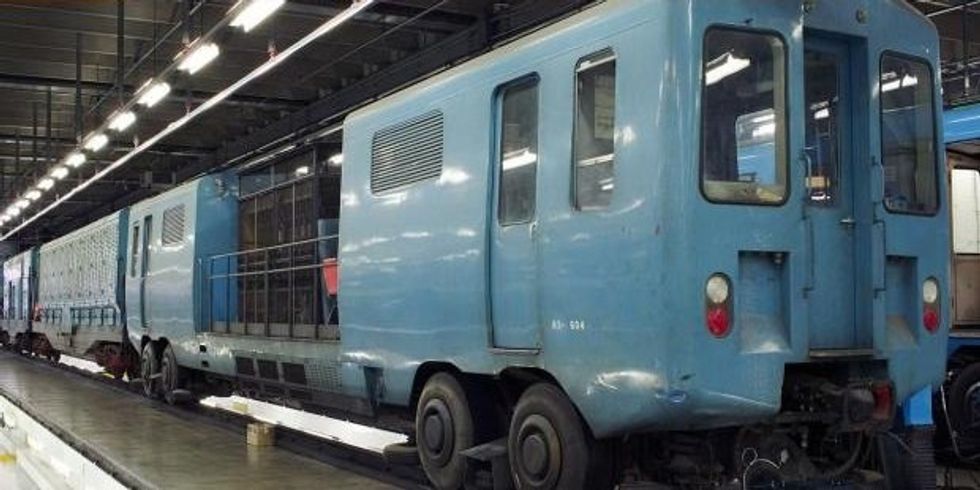 An odd looking metro car sits with a giant vacuum attached in a storage facility, ready to clean the tracks.