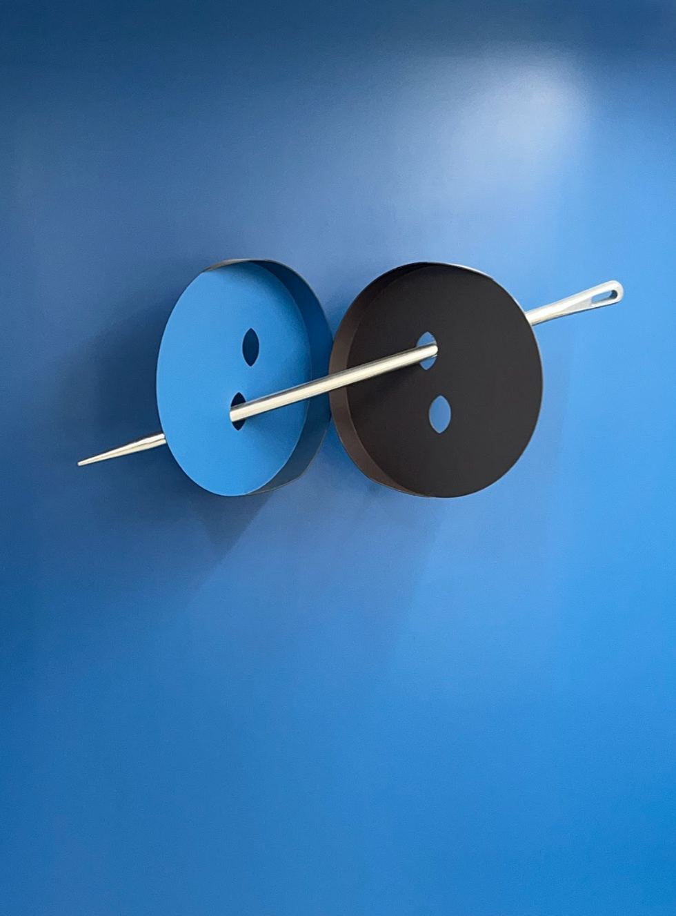 An oversized needle goes through two buttons in a confusing 3d configuration.