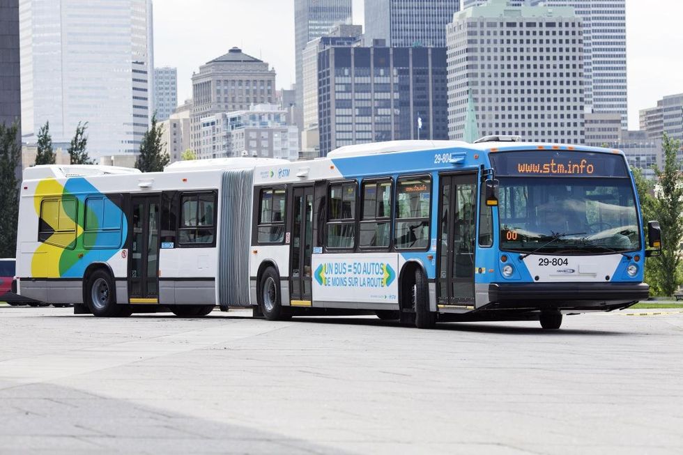 An STM bus on the road with Montreal's downtown skyline in the background.