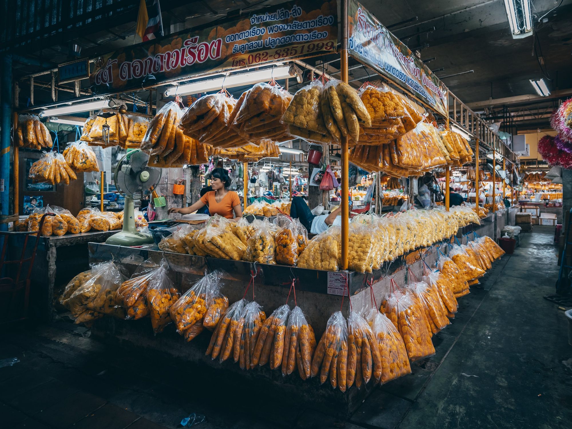 Bags of food hang off of a Bangkok street market stall at night.