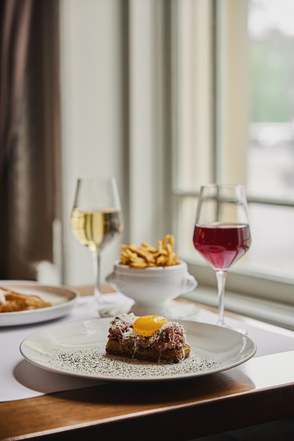 Beef tartare topped with egg yolk, served with fries and wine at a Montreal restaurant by the window.