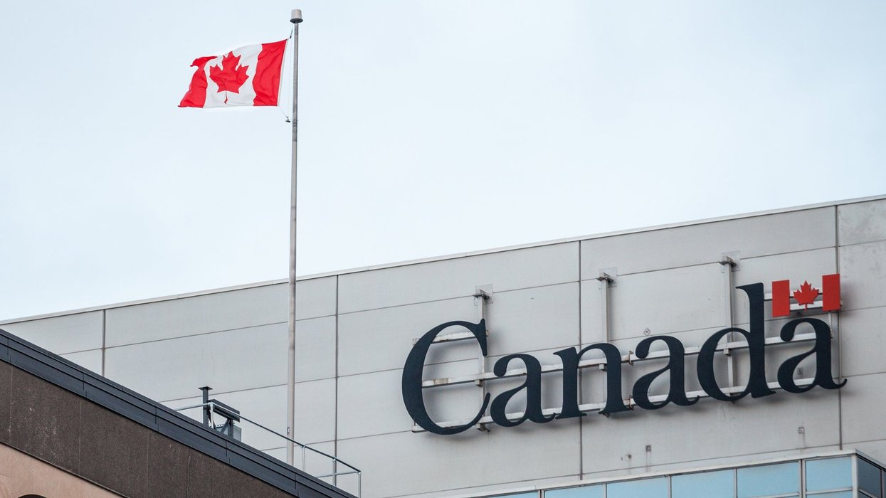 Canada Wordmark, the official logo of the Canadian government, on an administrative building next to a Canadian flag waiving.Canada Wordmark, the official logo of the Canadian government, on an administrative building next to a Canadian flag waiving.