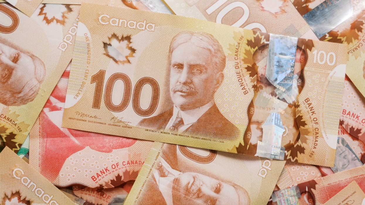 Close up of Canadian one hundred dollar bills spread out. Multiple Canadian 100 dollar bills with a portrait of Robert Borden, maple leaf holograms, and detailed security features visible.