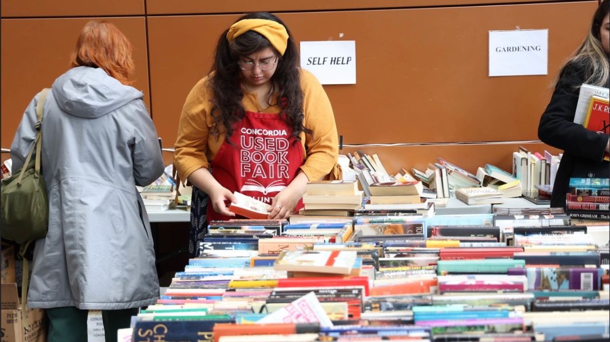 Concordia University used book fair with hundreds of books scattered across tables while a volunteer organizes books.