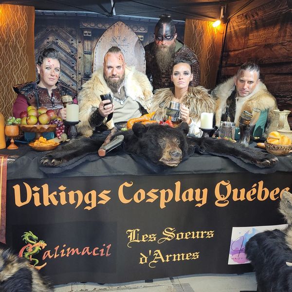 Cosplayers dressed like Vikings pose at a table covered in goblets and a bear skin.