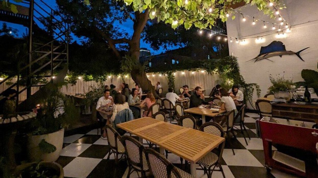 Diners eat outside on a checkered black and white patio by a spiral staircase and under fairy lights.