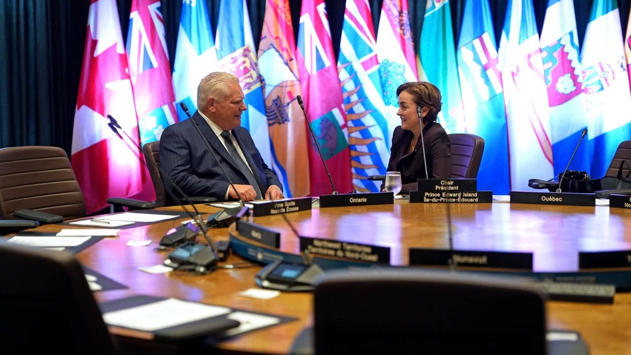 Doug Ford and Christine Fréchette talk at a meeting table with provincial and territorial flags behind them.