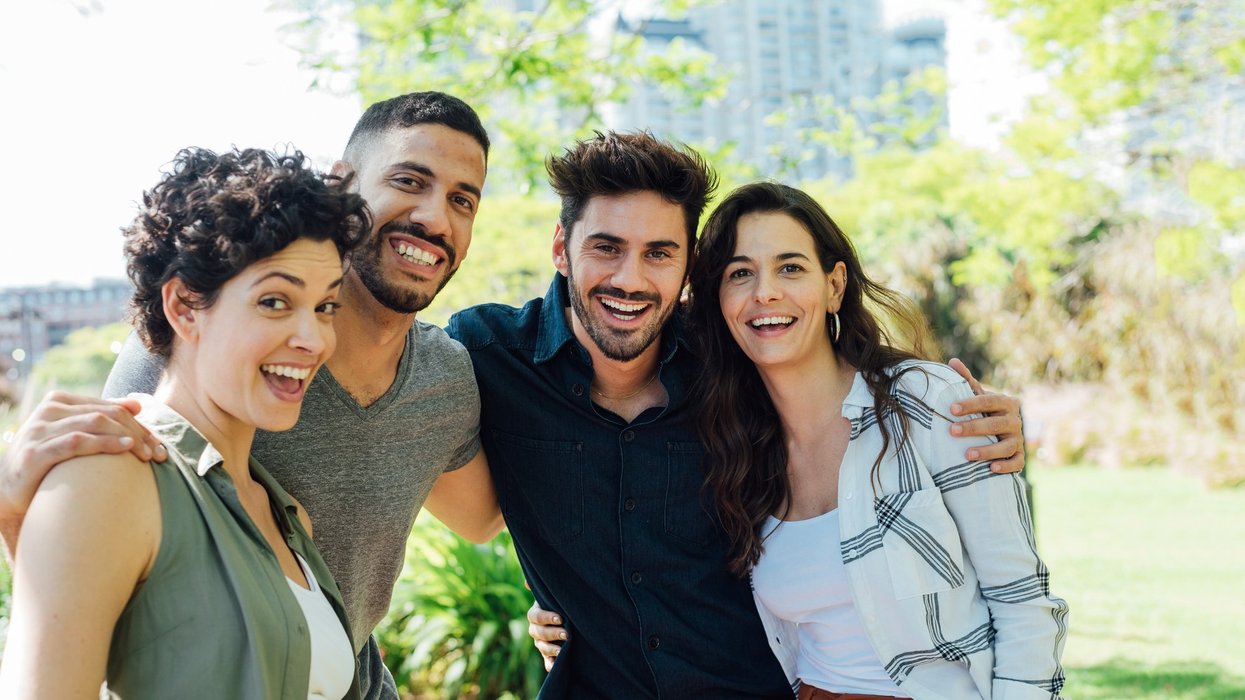 Four smiling adults posing together in a park on a sunny day