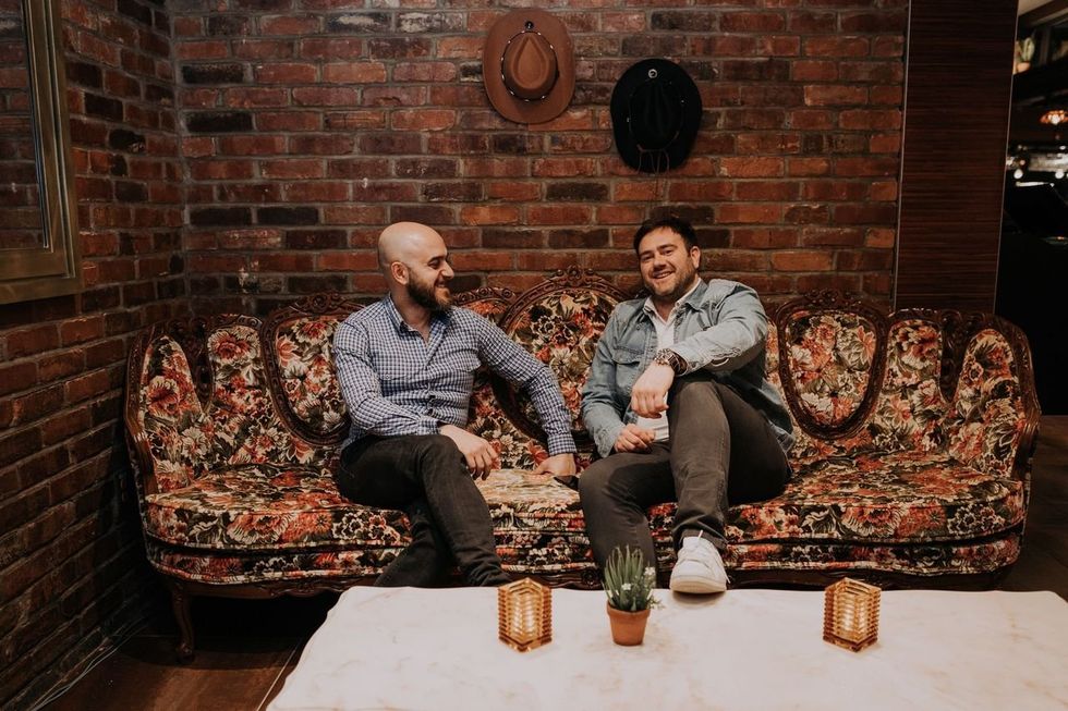 Franchisee Moussa Farha and Lawrence Picard sit on the couch at Jack Saloon Crescent, as cowboy hats hang from the exposed brick wall behind them.