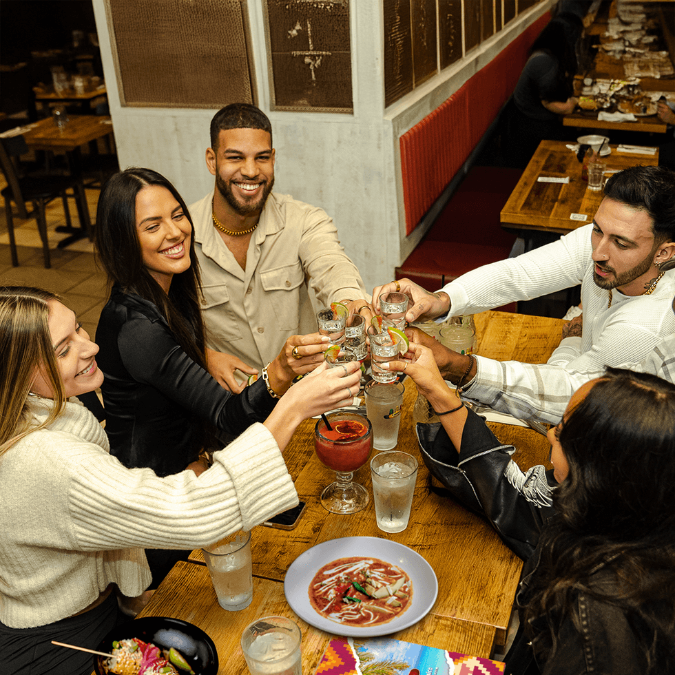Friends raising their cocktails over Mexican food at a restaurant.