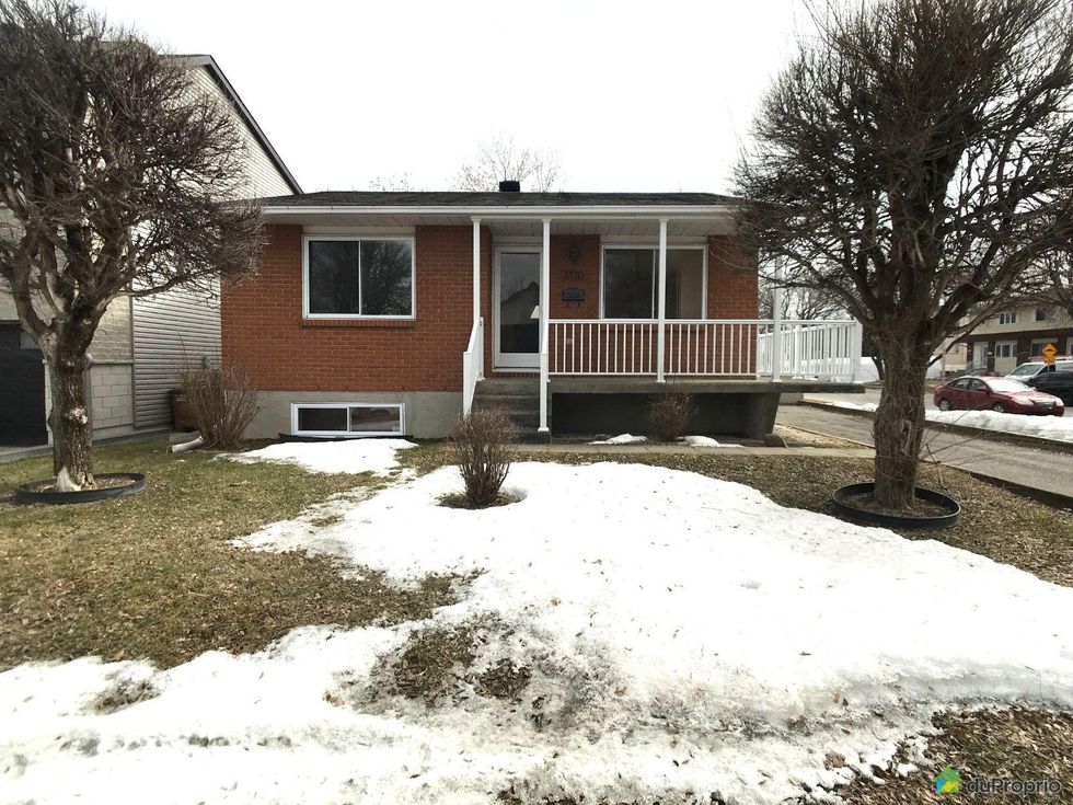 Front of a small brick house with a front porch in Laval, Quebec.