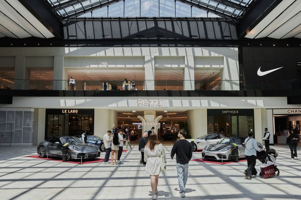 Luxury sports cars displayed inside Royalmount shopping mall with people walking around