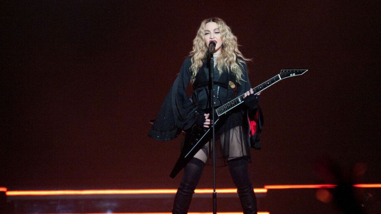 Madonna sings on stage with an electric guitar.