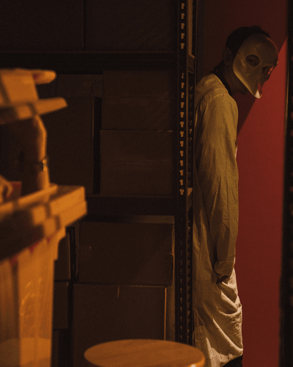 Masked figure standing in a dimly lit room during an immersive escape room experience.